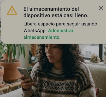 Una mujer sentada en un sofá mirando un teléfono móvil con una notificación de advertencia de almacenamiento lleno para WhatsApp en la parte superior de la pantalla
