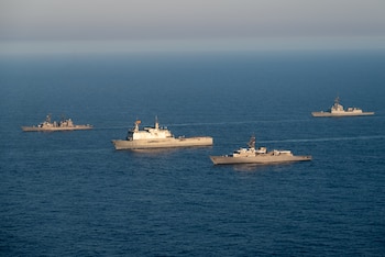 Cuatro buques de guerra navegan en aguas oceánicas bajo un cielo despejado. Uno de los buques lleva izada una bandera de España