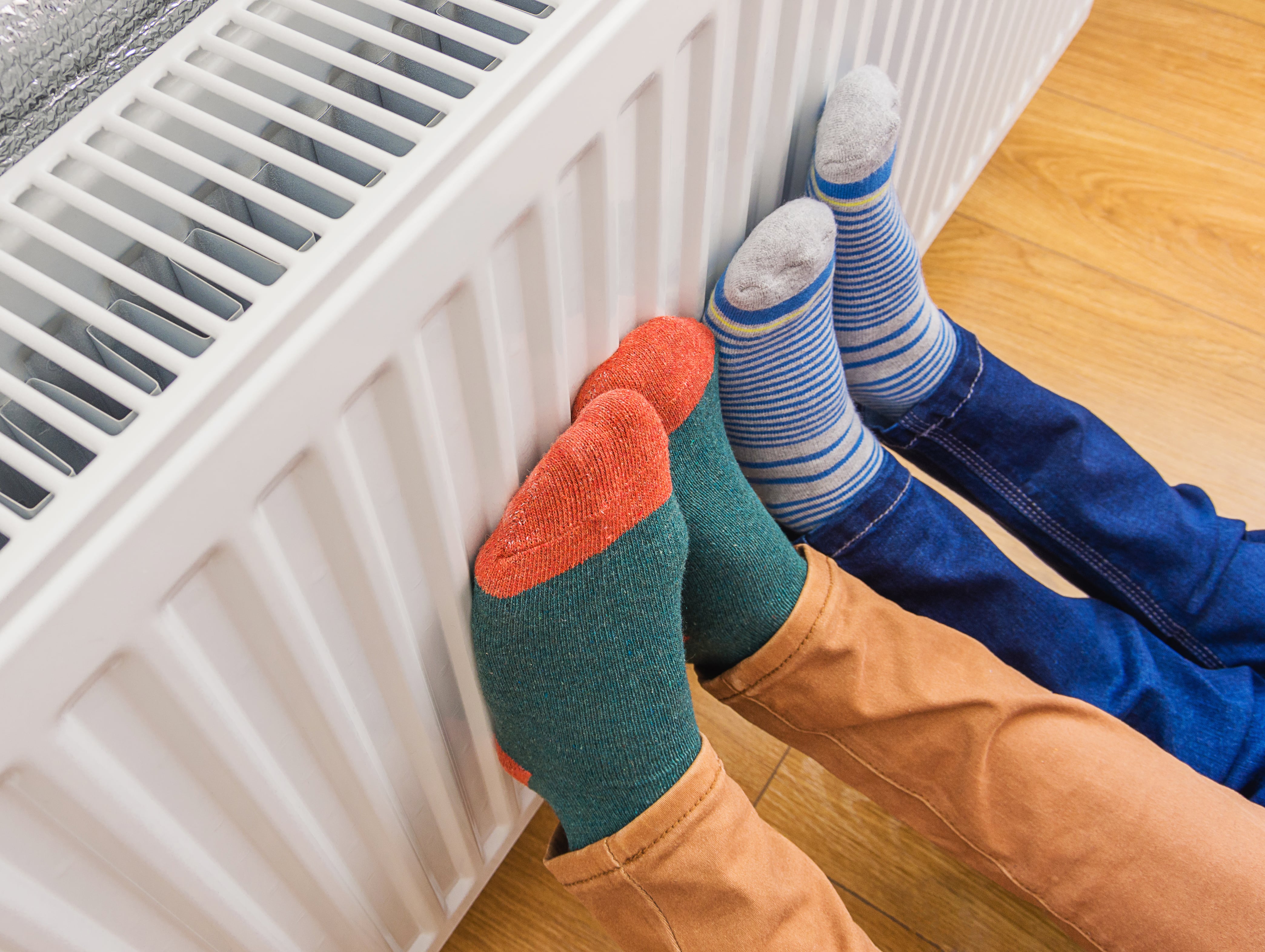 Unos niños se calientan los pies con un radiador. (Adobe Stock)