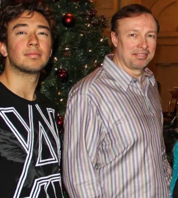 Dos hombres posan de pie junto a un árbol de Navidad decorado con esferas rojas
