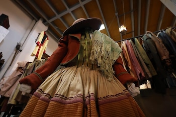 Maniquí con falda larga de capas, chaqueta, rebozo y sombrero frente a percheros con diversa vestimenta en un almacén