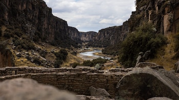 Un cañón con paredes rocosas verticales, un río en el fondo y un muro de piedra en primer plano