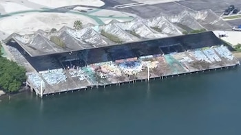 Vista aérea de un complejo de gradas junto al agua, con cubierta de picos, asientos de cemento con marcas de color, muelles y una zona pavimentada