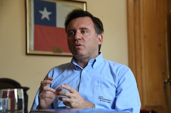 Un hombre con camisa azul con el bordado de la Ilustre Municipalidad de Punta Arenas gesticula frente a un cuadro de la bandera de Chile