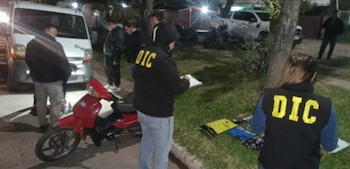 Agentes con chalecos que llevan la sigla DIC inspeccionan una motocicleta roja y diversos objetos colocados sobre el césped junto a una furgoneta