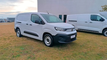 Una van comercial blanca Citroën Berlingo estacionada sobre césped verde, con un edificio moderno de fondo y otra van similar al costado
