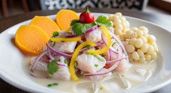 Plato blanco con ceviche de pescado, cebolla morada, ají amarillo, rocoto rojo, cilantro, camote cocido, granos de choclo y leche de tigre con hielo.