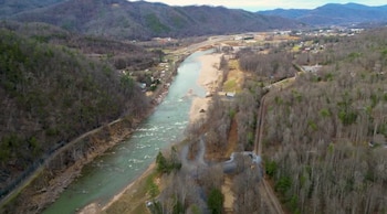 Vista aérea de un valle montañoso con un río ancho fluyendo por el centro. Hay orillas de arena expuesta, árboles sin hojas, y carreteras que atraviesan la zona