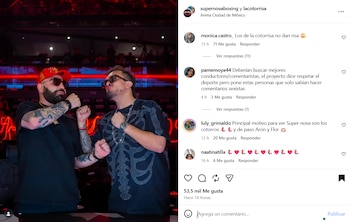 Dos hombres en un escenario con iluminación roja, uno con barba y gorra roja, el otro con bigote y camiseta de esqueleto, ambos con gafas de sol y puños cerrados