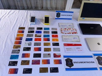 Objetos incautados sobre una mesa blanca: decenas de tarjetas de crédito de diversos bancos, dos teléfonos móviles, dos laptops, un monitor y sobres de documentación bancaria