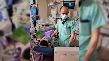 Un sanitario con mascarilla y bata verde maniobra junto a una incubadora y un monitor digital en una sala médica