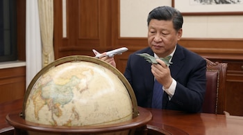 El presidente chino Xi Jinping, vestido con traje oscuro, sostiene un avión de pasajeros blanco y un avión de combate verde, frente a un globo terráqueo en una mesa de madera.