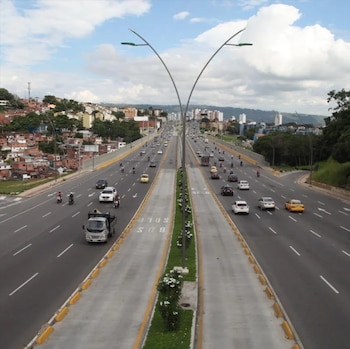 Vista de una autopista de varios carriles con autos, motocicletas, taxis amarillos y carriles marcados para autobuses