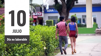 Un hombre y una mujer de la mano caminan por una acera junto a arbustos, con edificios y un banco al fondo. Una gráfica sobrepone el texto 10 JULIO Día no laborable.