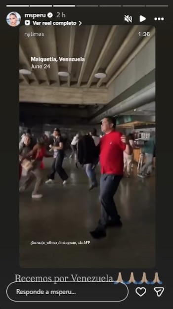 Una multitud de personas se mueve en el interior de un edificio, algunas mirando hacia arriba. Hombre con camisa roja y jeans en primer plano. Se ve interfaz de red social