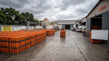 Decenas de balones de gas anaranjados de Solgas en palés, tanques industriales y una pizarra de inventario en una planta.
