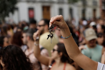 Una mano sostiene en alto un manojo de llaves frente a una multitud de personas desenfocadas en una calle