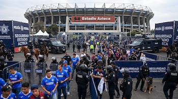 Exterior del Estadio Azteca con personal de la Policía Federal, vehículos, caballos, un perro policía y aficionados de los equipos Cruz Azul y Atlante.