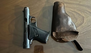 Vista superior de una pistola de color oscuro y una funda de cuero marrón desgastada, ambas sobre una superficie de madera oscura