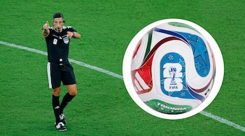 Un árbitro con uniforme negro en un campo de fútbol verde señalando, junto a un primer plano de la pelota blanca Trionda del Mundial 2026 con patrones rojos, azules y verdes.