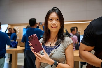 Una mujer sonriente sostiene un teléfono móvil de color rojo en una tienda con clientes y empleados