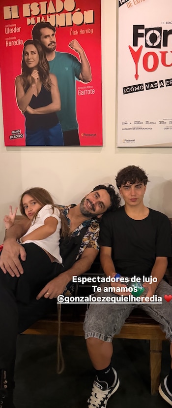 Gonzalo Heredia sonríe sentado en un banco con sus dos hijos, un niño y una niña, frente a un cartel de la obra 'El estado de la unión'