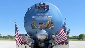 Parte trasera de un camión cisterna azul con tres figuras de hombres en uniforme militar y el texto "Solo se carga". Dos banderas de Estados Unidos cuelgan a los lados