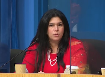 Lubby Navarro, una mujer con cabello oscuro y blusa roja, sentada detrás de una mampara de cristal en un entorno de sala de audiencias