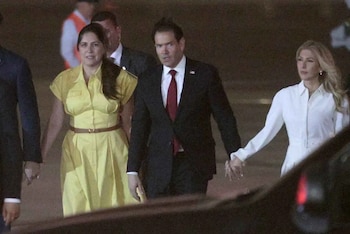 Marco Rubio viste traje oscuro y corbata roja mientras camina de noche junto a dos mujeres, una vestida de amarillo y otra de blanco
