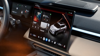 Interior de un automóvil con volante, tablero, rejillas de ventilación y una pantalla táctil central que exhibe un vehículo digital, música y aplicaciones