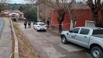 Vehículo oficial plateado con logotipo MPF, automóvil blanco, varias personas con uniforme, cinta de seguridad blanca, casas y árboles en una calle