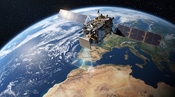 Un satélite con paneles solares desplegados proyecta una cuadrícula luminosa hacia la superficie de la Tierra vista desde el espacio.