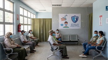 Sala de espera con personas sentadas usando mascarillas y manteniendo distancia. Un cartel del Ministerio de Salud Pública de República Dominicana es visible.
