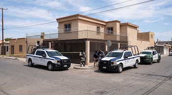 Tres patrullas de seguridad y agentes armados permanecen frente a una casa de dos pisos delimitada con cinta de precaución.