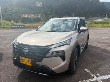 Un automóvil SUV de color beige claro estacionado sobre asfalto con una placa amarilla y montañas de fondo