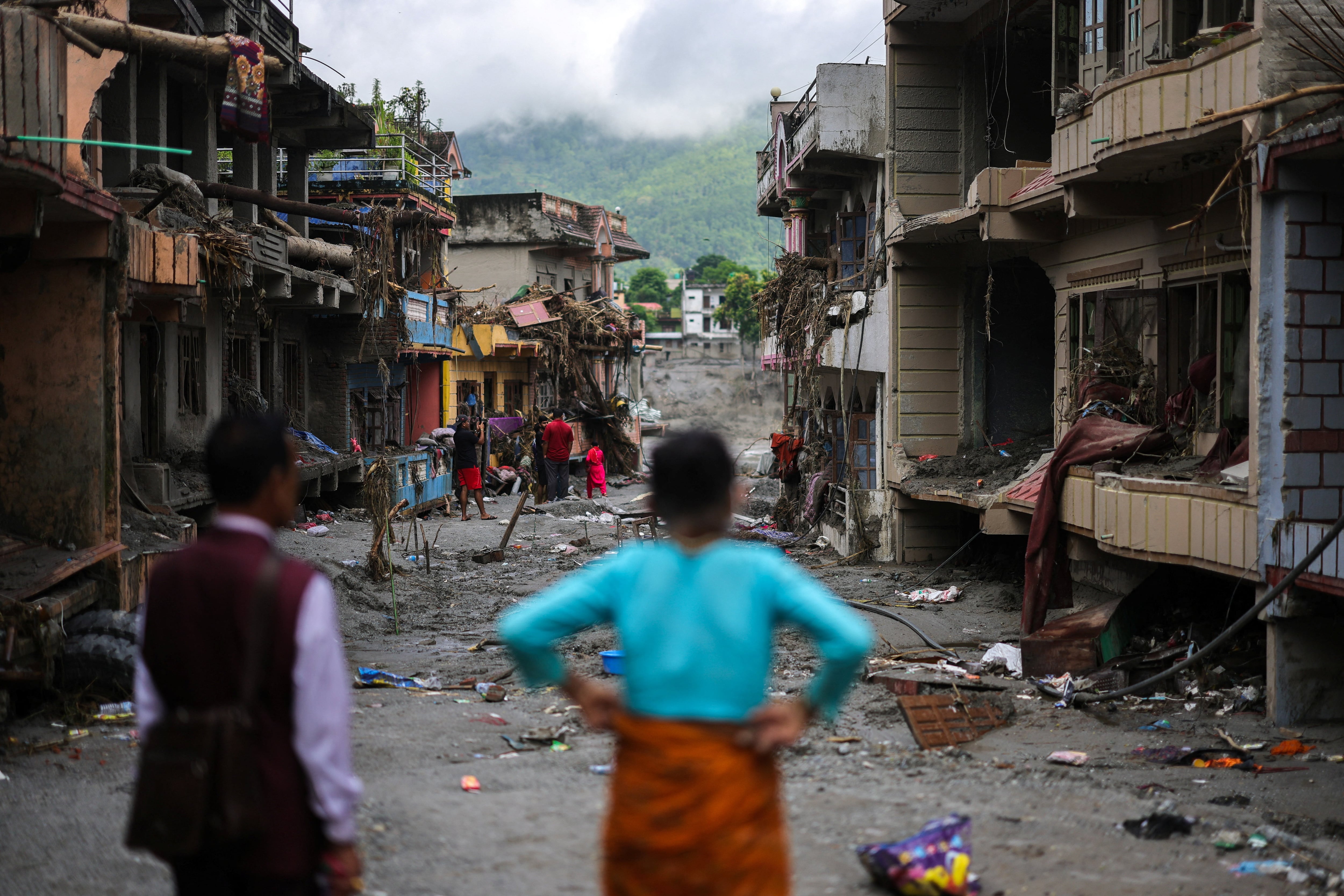 Personas caminan junto a edificios y casas dañados y cubiertos de lodo tras mortales inundaciones repentinas y deslizamientos de tierra, en Devighat, distrito de Nuwakot, Nepal (REUTERS/Athit Perawongmetha)