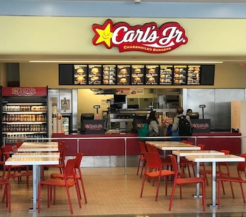 Interior de Carl's Jr Los Ángeles: logo, menú, mostrador con clientes, refrigerador de bebidas y zona de comedor con mesas y sillas rojas