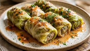 Rollos de repollo rellenos con carne y arroz, bañados en salsa de tomate y perejil picado, dispuestos en un plato cerámico rústico bajo luz natural cálida