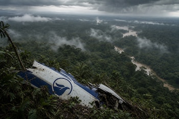 Un resto de ala de avión con un logotipo azul sobre la vegetación de una selva con un río y nubes densas de fondo.