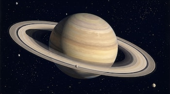 El planeta Saturno con sus anillos prominentemente visibles, cuatro lunas pequeñas y un fondo de espacio profundo salpicado de estrellas.