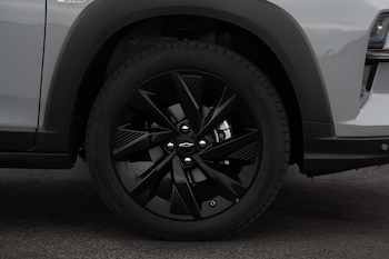 Primer plano de la rueda delantera izquierda de un Chevrolet Sonic gris claro, mostrando la llanta de aleación negra, el neumático Bridgestone y parte del guardabarros