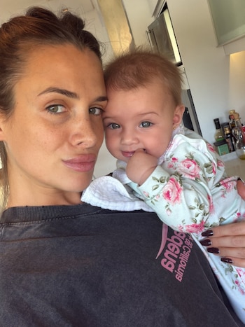 Cami Homs sostiene a su bebé vestida con ropa de estampado floral mientras ambas miran hacia la cámara