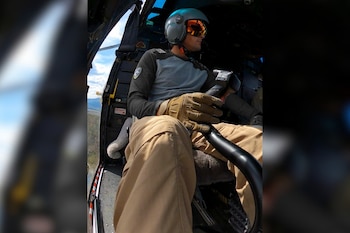 Un piloto con casco, visera de protección y guantes sostiene la palanca de control dentro de la cabina de un helicóptero