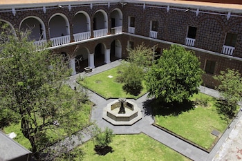 Vista aérea de un patio interior con jardín, senderos, fuente octogonal y árboles. Rodeado por un edificio de dos pisos con arcos y paredes con patrones