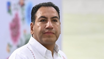 Primer plano de un hombre maduro con cabello oscuro y camisa blanca bordada sobre un fondo claro de tonos suaves
