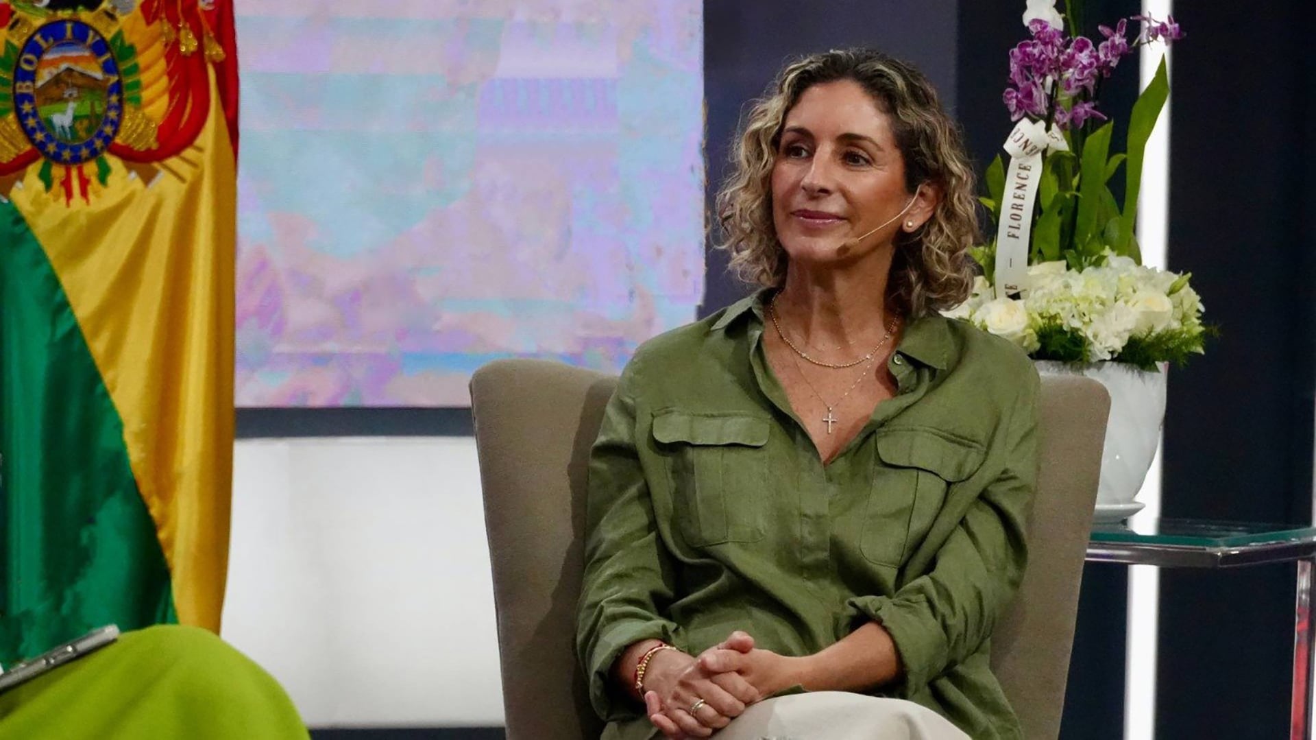 La primera dama de Bolivia permanece sentada en un estudio de televisión junto a la bandera nacional.
