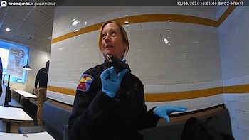 Una agente de policía con guantes azules sostiene un cargador de balas dentro de un restaurante de comida rápida con paredes de azulejos