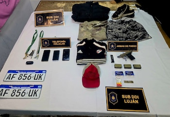 Una mesa blanca exhibe armas, municiones, celulares, llaves, ropa, calzado, gorra, y dos matrículas de Argentina con la inscripción 'AF 856 UK', junto a carteles policiales