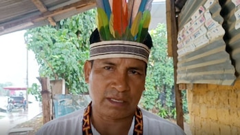 Retrato de un hombre de cabello oscuro con una corona de plumas multicolores y una cinta con motivos geométricos sobre el cuello