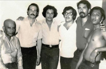 Retrato de Lady M, una mujer de cabello castaño corto y gafas, vestida con una camiseta de rayas y un collar dorado con una cruz, sentada al aire libre